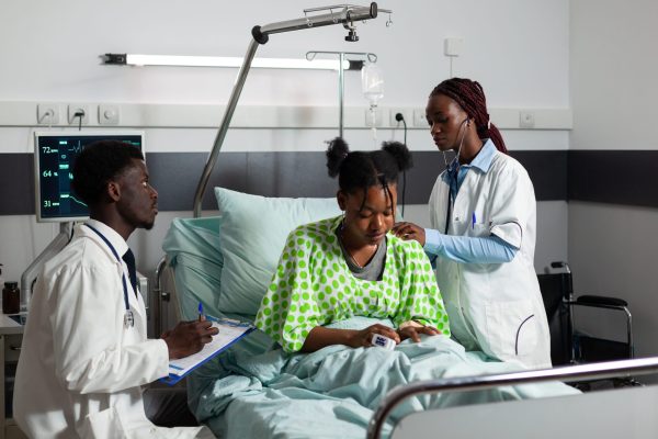 african-american-therapist-doctor-listening-patient-lungs-using-stethoscope-discussing-medical-expertise-with-therapist-sick-young-woman-resting-bed-recovering-after-surgery-hospital-ward-min